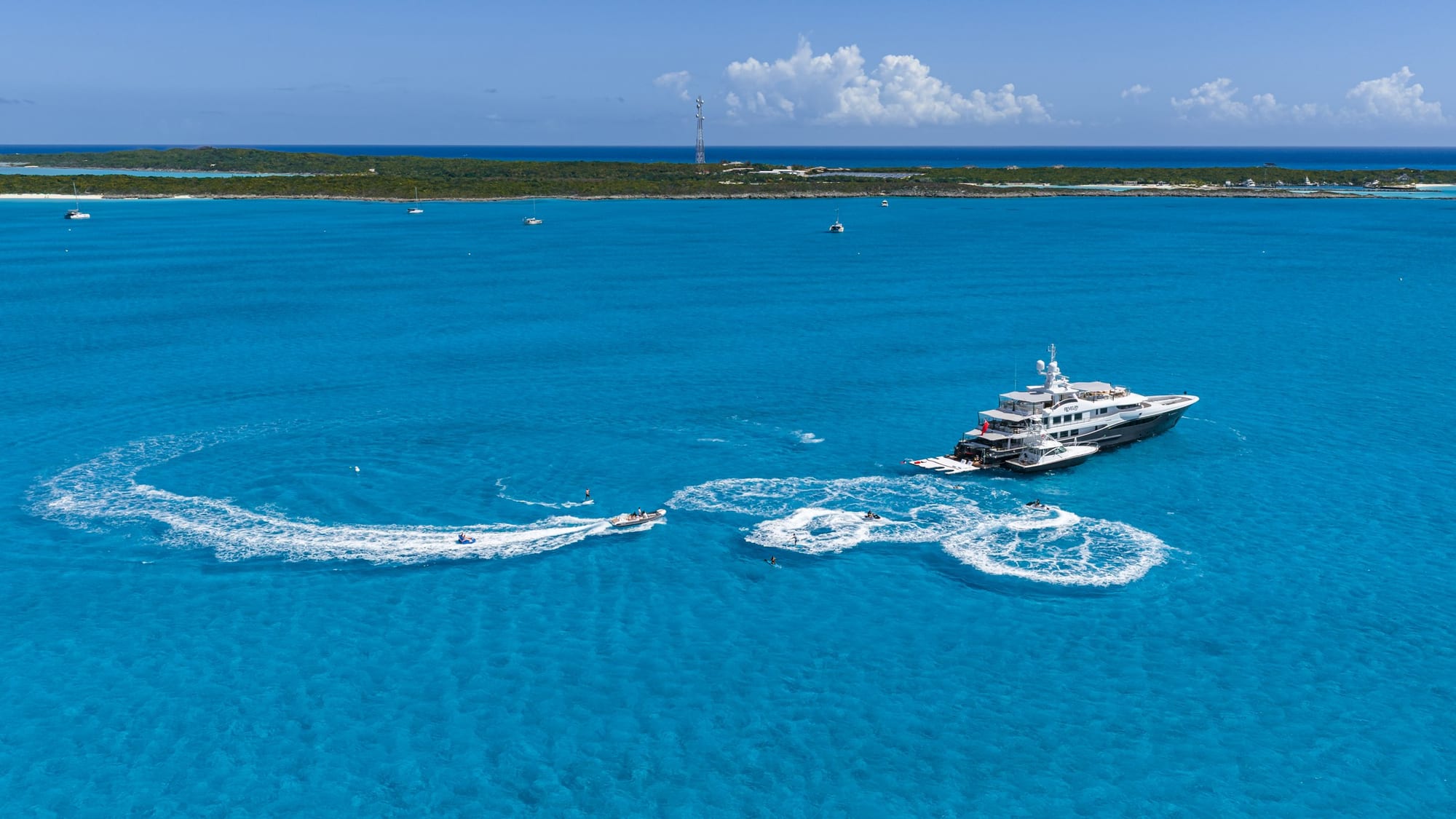 Superyacht anchored on shallow turquoise water with a tender wake looping around her