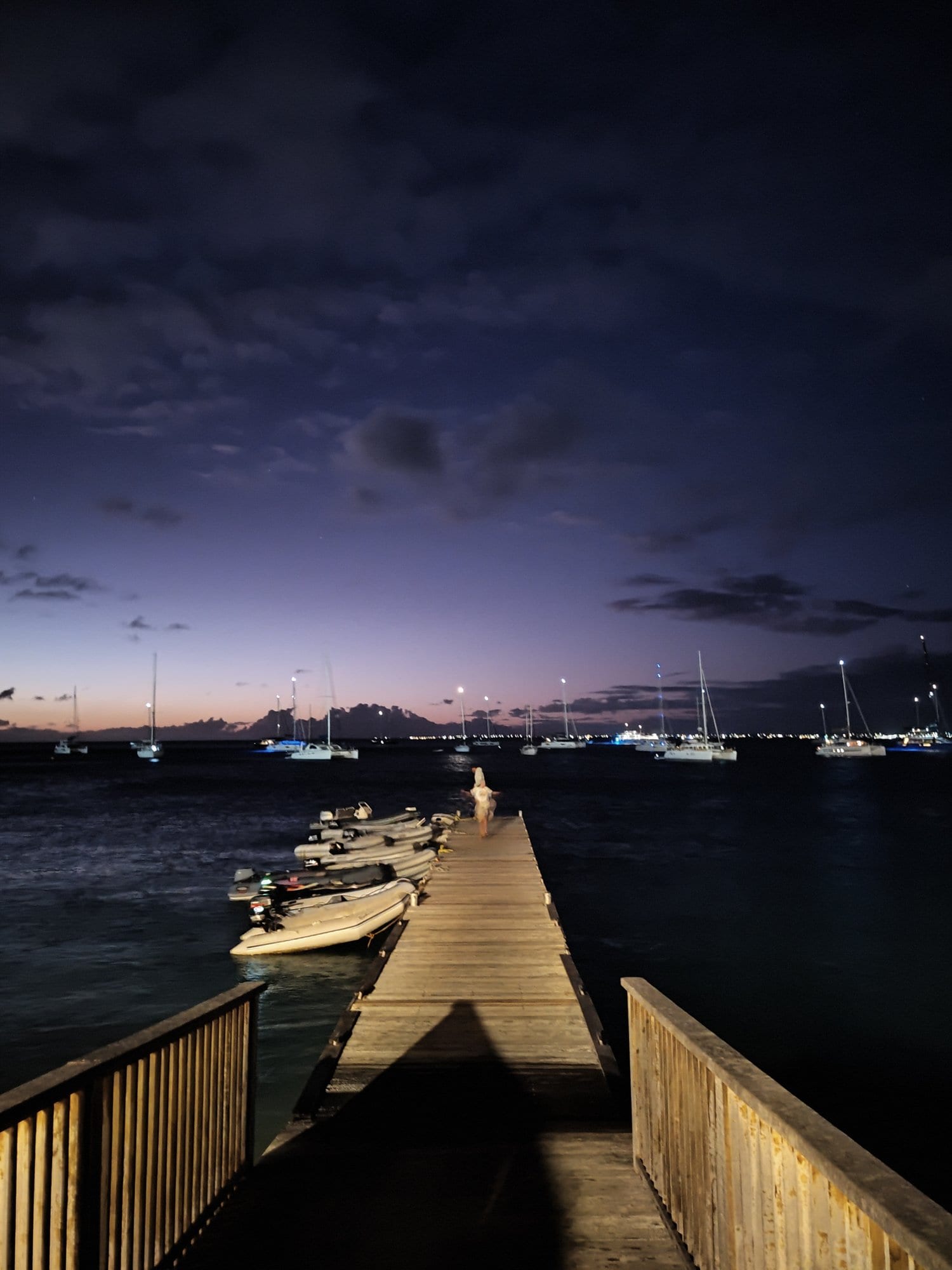 Wooden jetty at night with yachts anchored in the bay