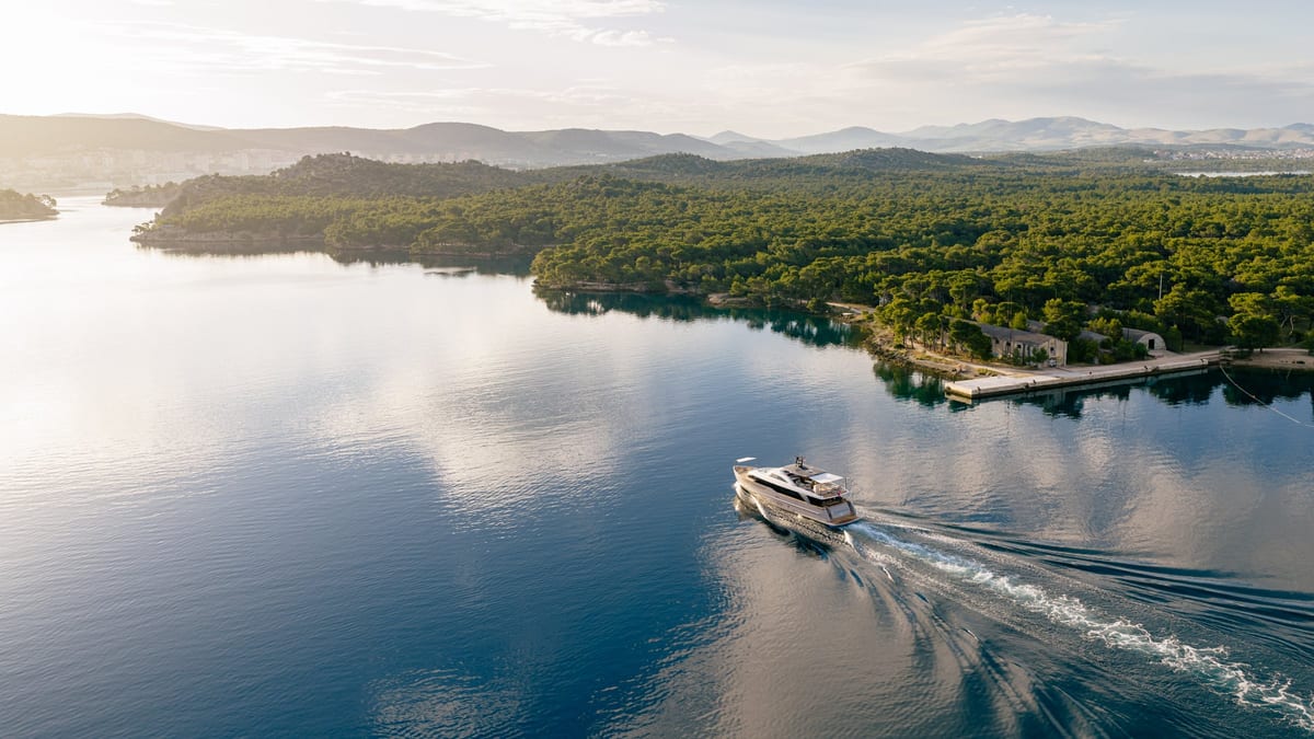 Yacht cruising across still water with its reflection and wake in soft evening light
