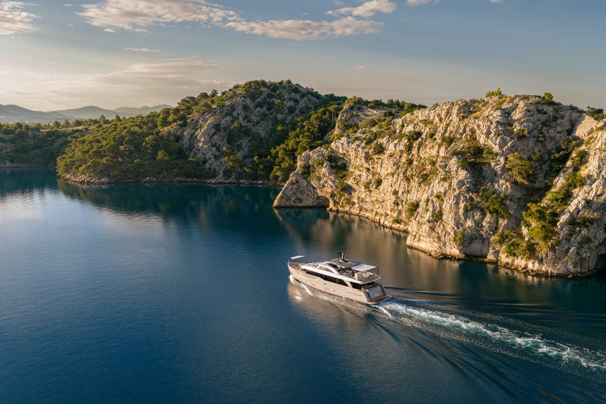 Yacht running along a calm channel beneath limestone cliffs at sunset