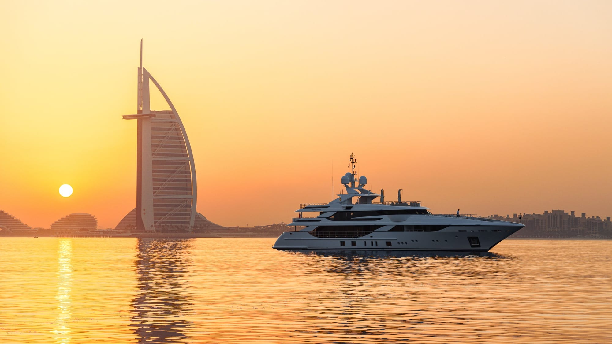 Superyacht passing the Burj Al Arab at sunrise on flat, golden water
