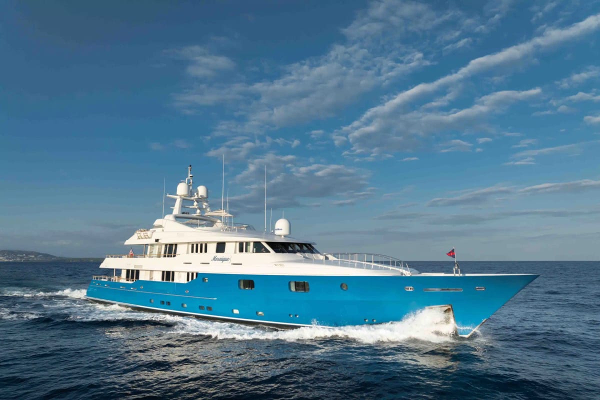Classic motor yacht with a bright blue hull cruising through open water.