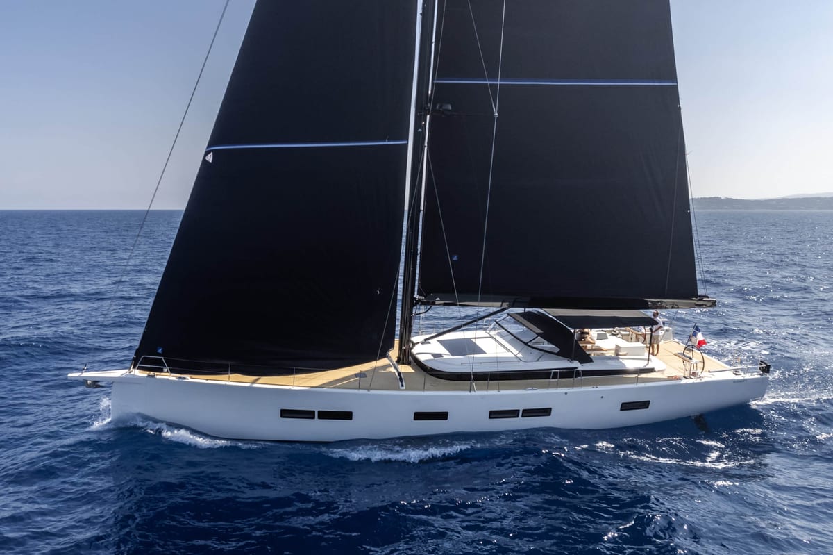 Aerial view of a large sailing yacht with dark sails on open sea.