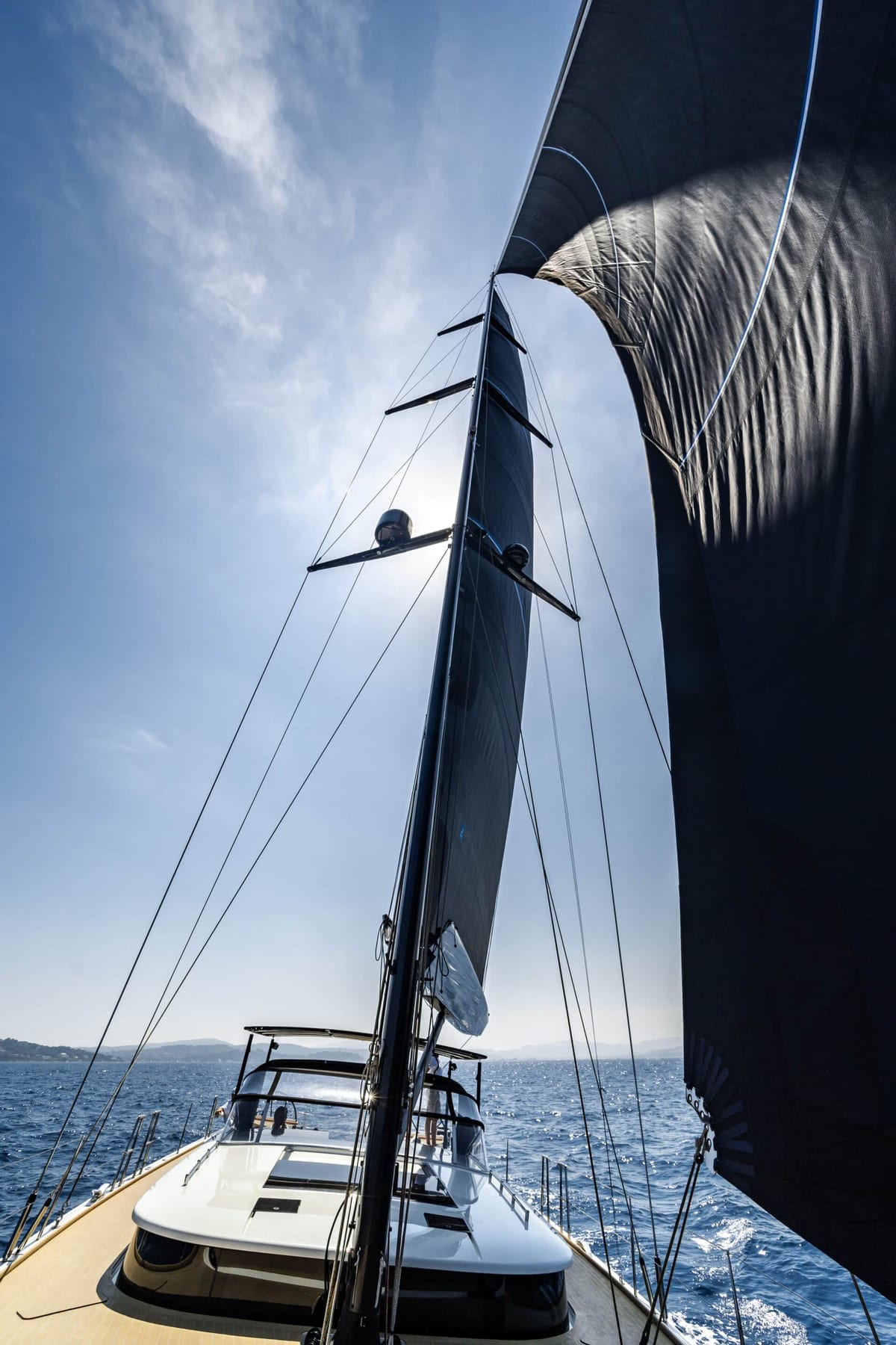 View from the deck of a sailing yacht under a dark sail on a sunny day.