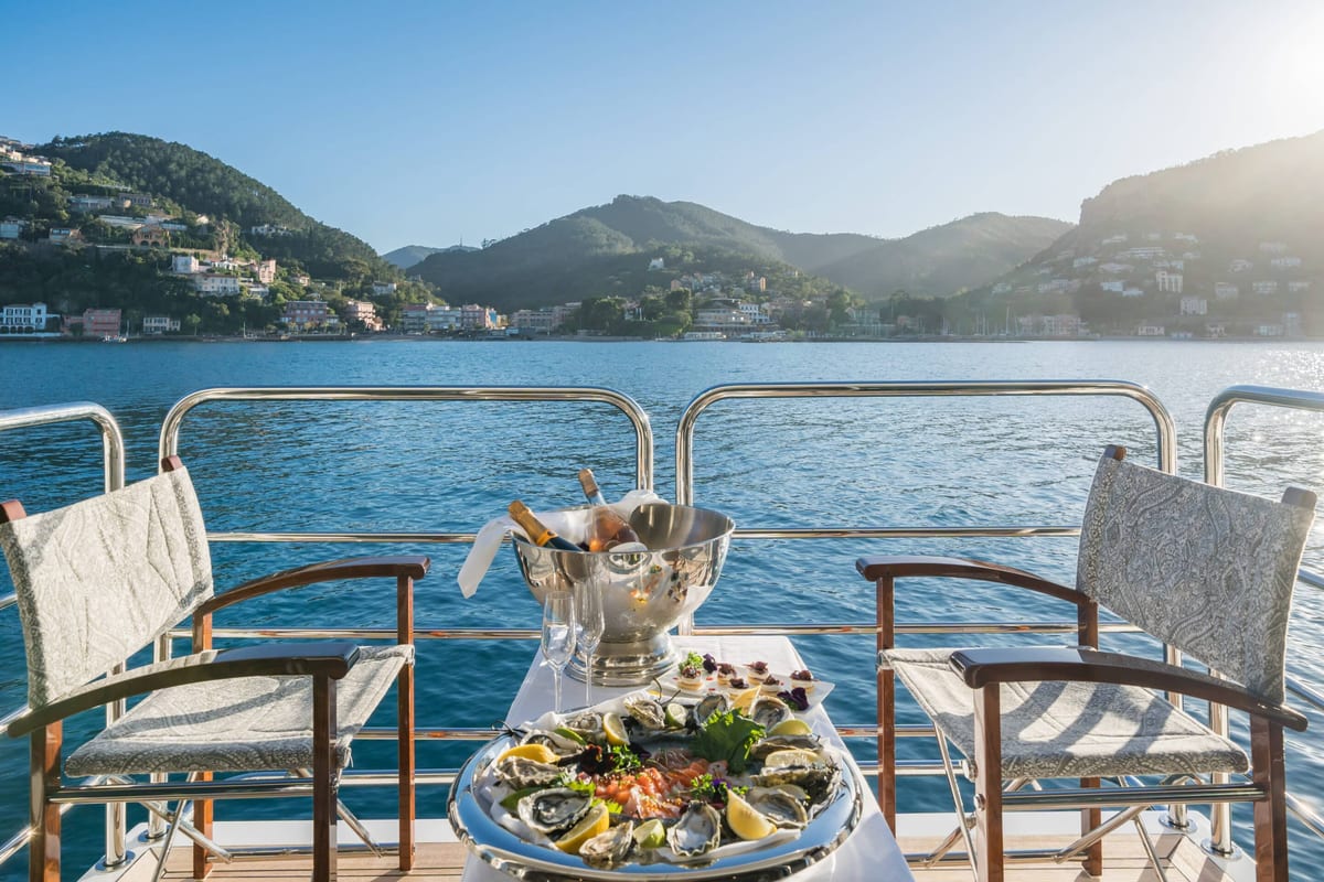 Oyster and seafood platter with champagne on a yacht deck overlooking a coastal village.