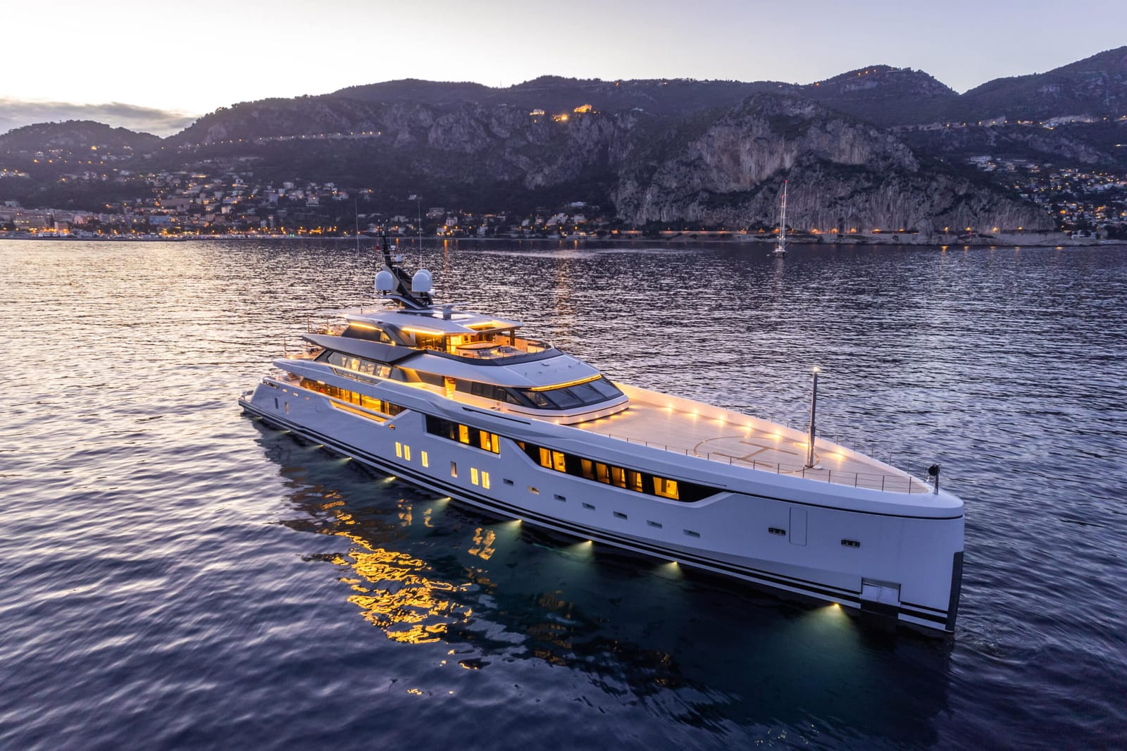 Superyacht at anchor at dusk with deck and underwater lights on