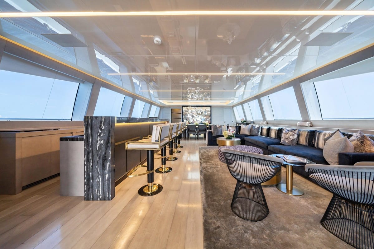 Yacht sky lounge with marble bar, tall bar stools, navy sofas and wraparound windows.