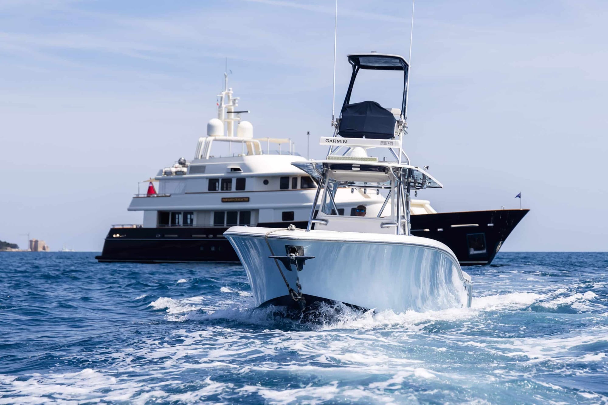Sport fishing tender running past a larger superyacht at anchor