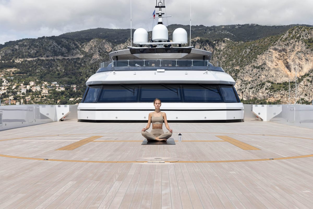 Woman meditating cross-legged on a superyacht helipad deck in front of the bridge and radar domes.